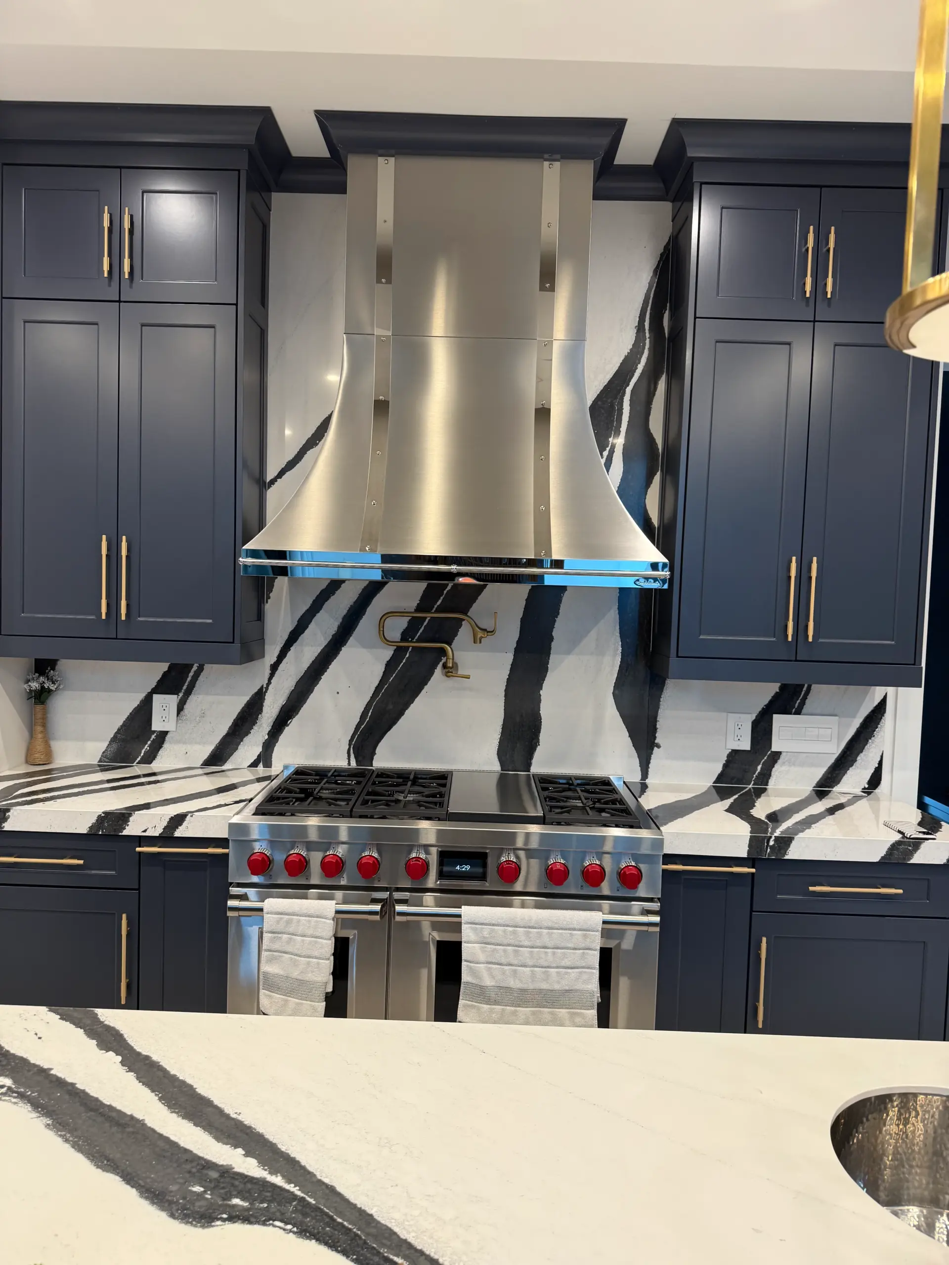 Close-up of gourmet kitchen range wall with navy cabinetry, marble backsplash and statement range hood